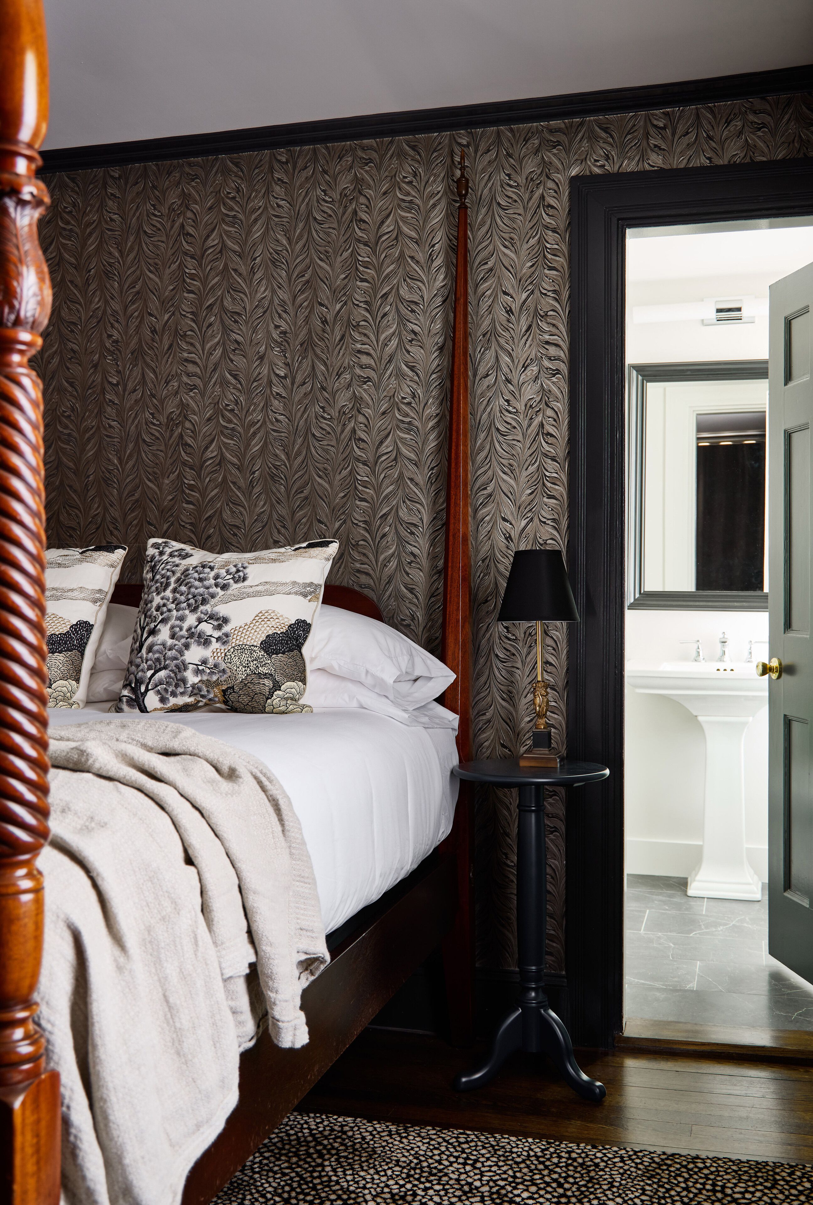 A bedroom with a bed, pillows, a bedside table with a lamp, and a door leading to a bathroom.