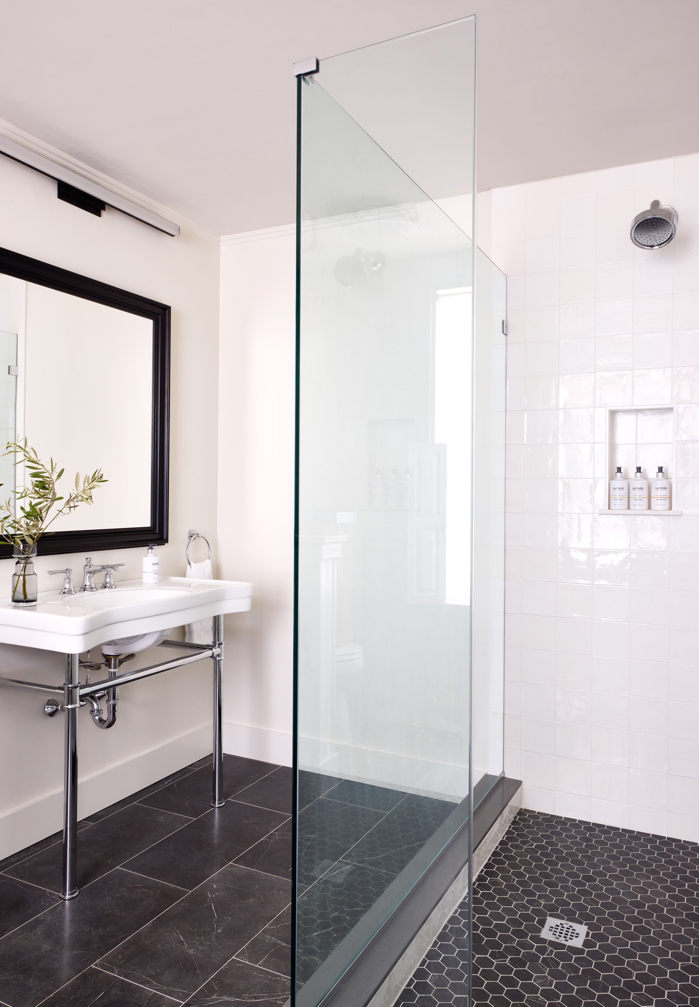 A modern bathroom with a glass-enclosed shower, a white sink with chrome fixtures, and a potted plant.