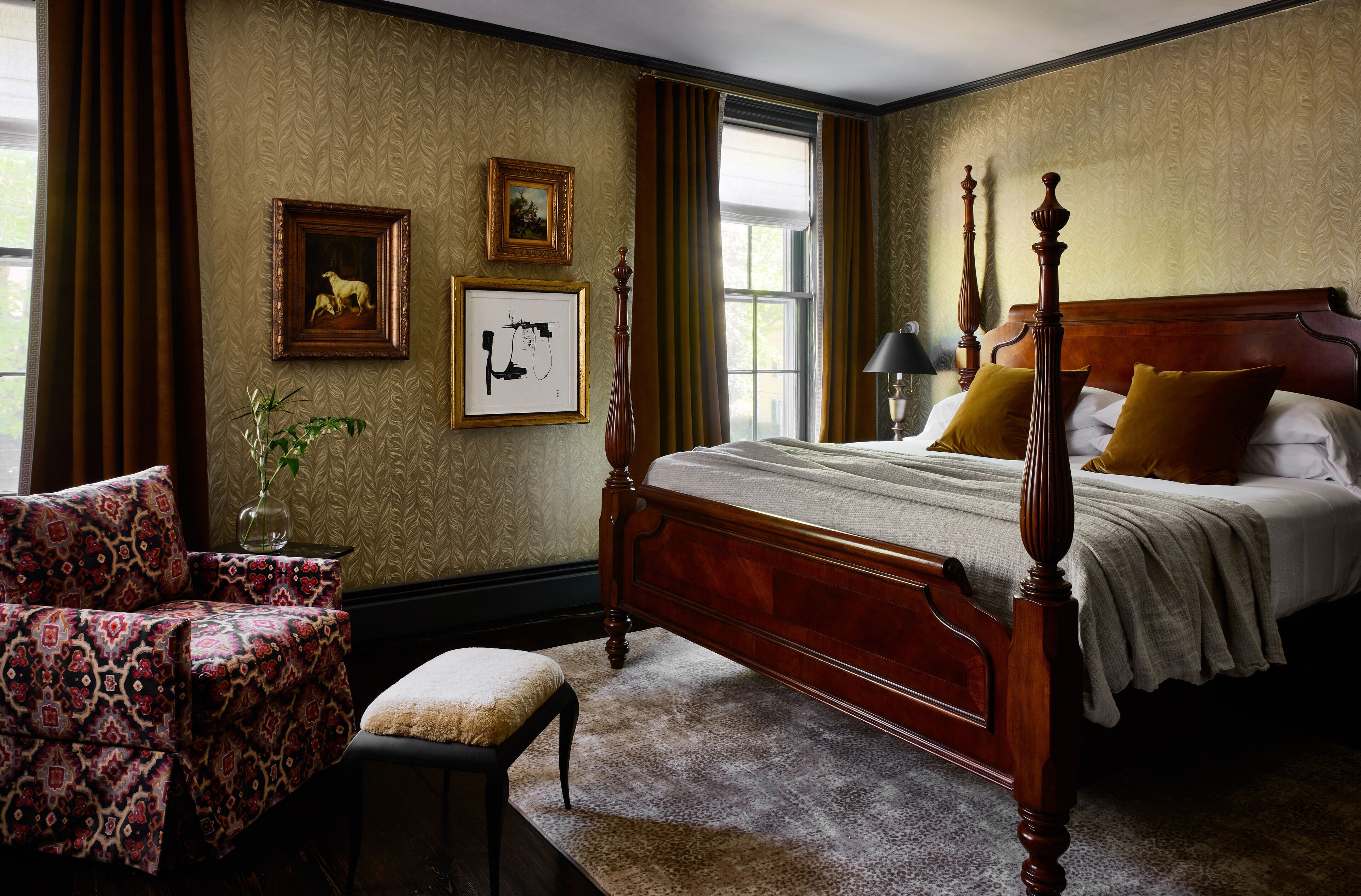 A bedroom with a four-poster bed, a chair, a vase with a plant, and framed pictures on the wall.