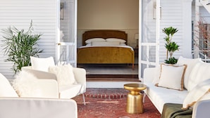 An open doorway leading to a bedroom with a bed, a white sofa, a round gold table, and a potted plant. - Kennebunkport Captains Collection (Kennebunkport)