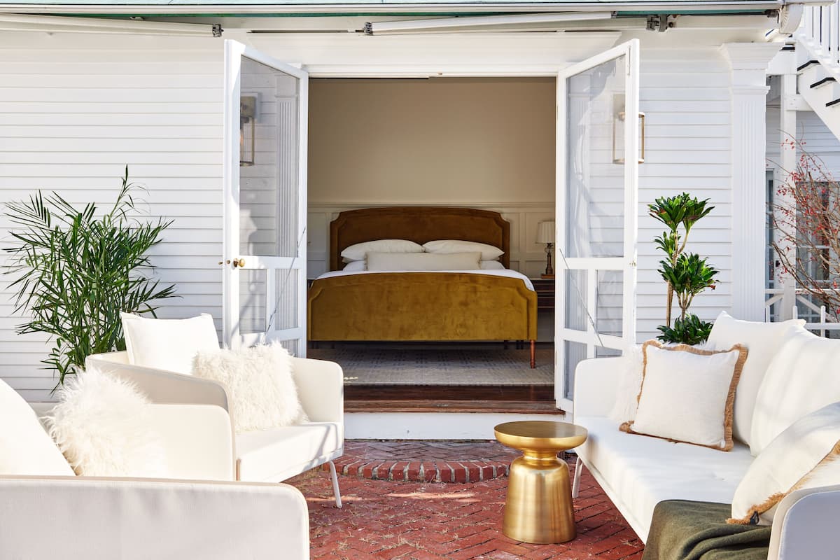 An open doorway leading to a bedroom with a bed, a white sofa, a round gold table, and a potted plant.