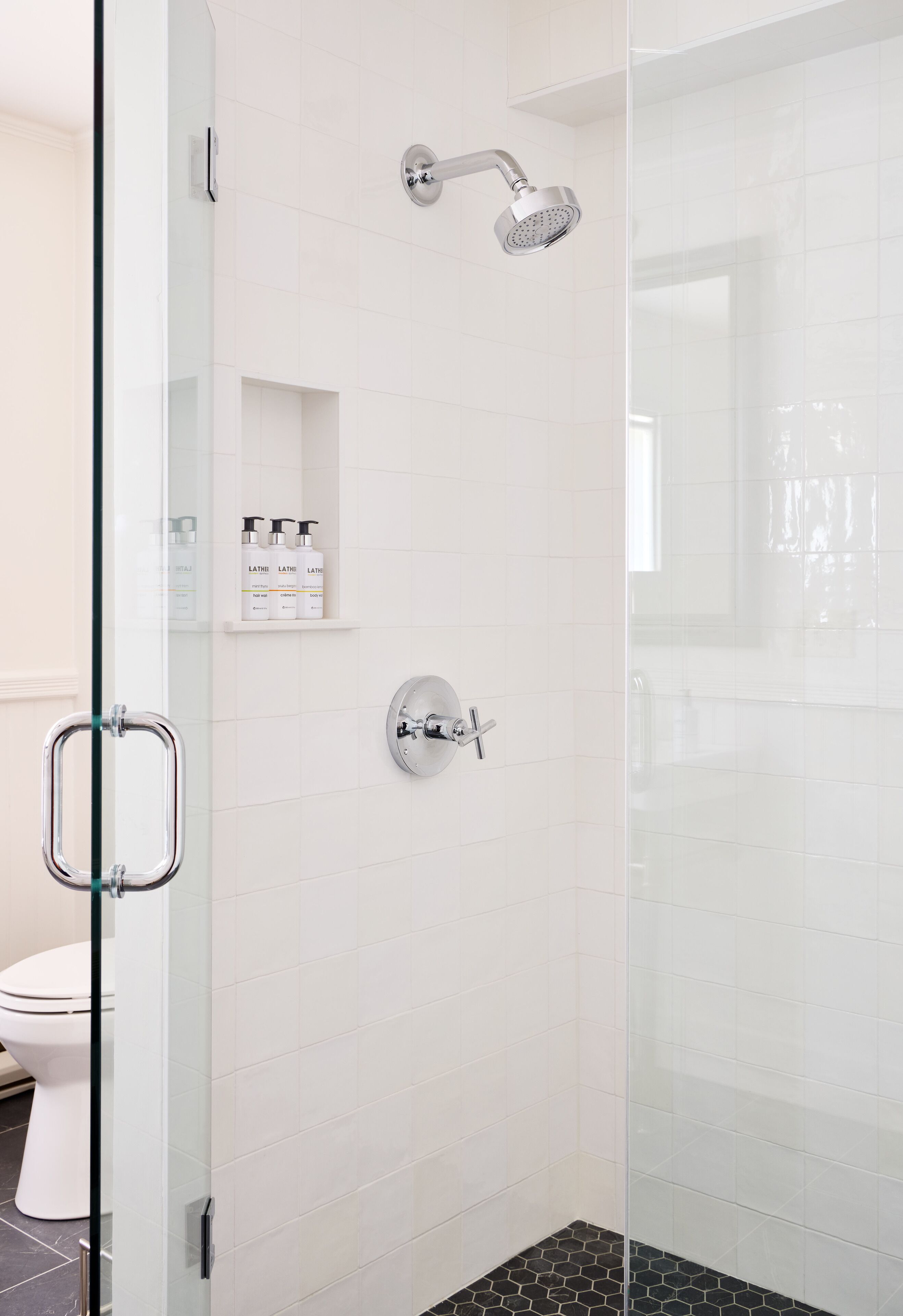 A modern bathroom with a glass shower enclosure, a toilet, and a shelf with toiletries.
