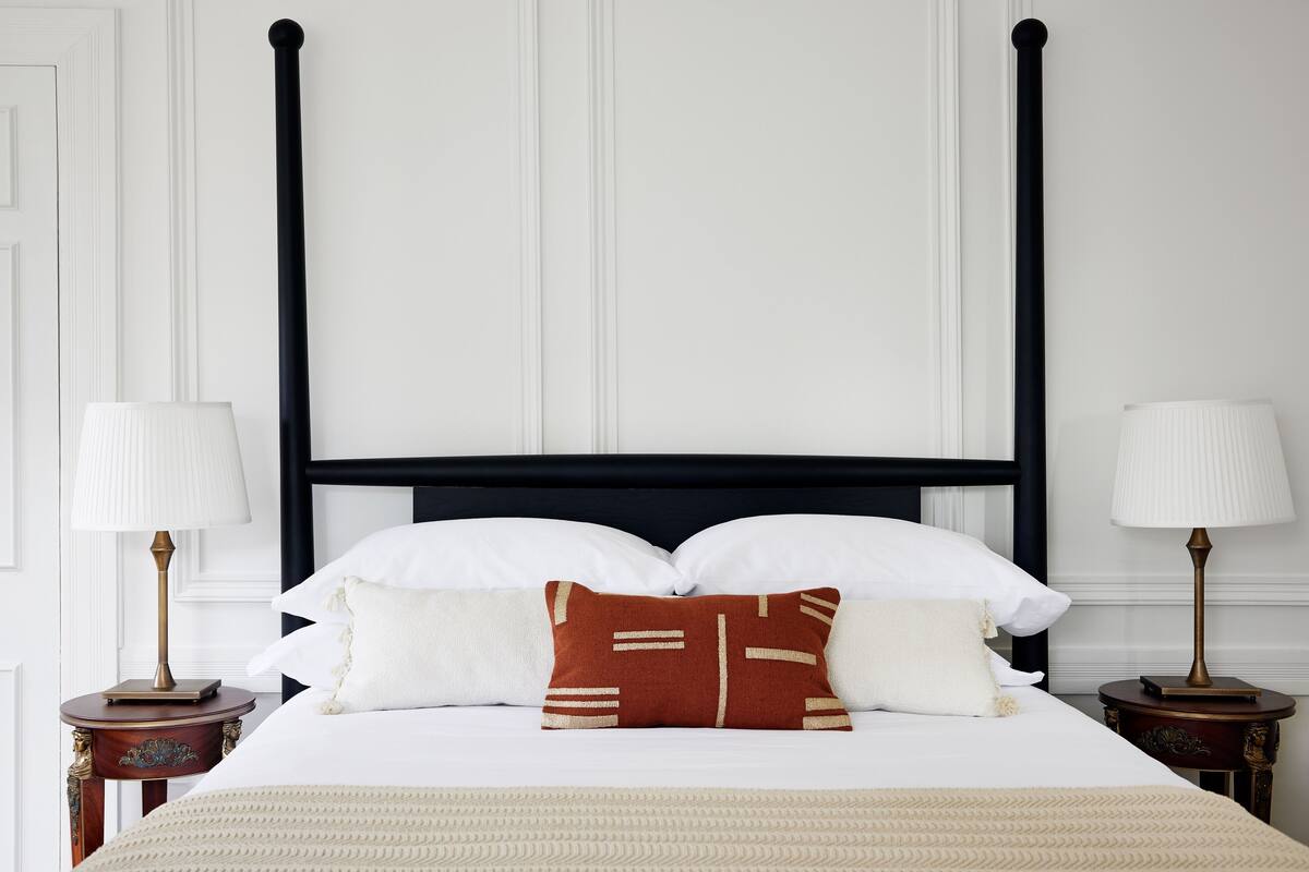 A neatly made bed with white and brown pillows, a black headboard, and two bedside tables with lamps.