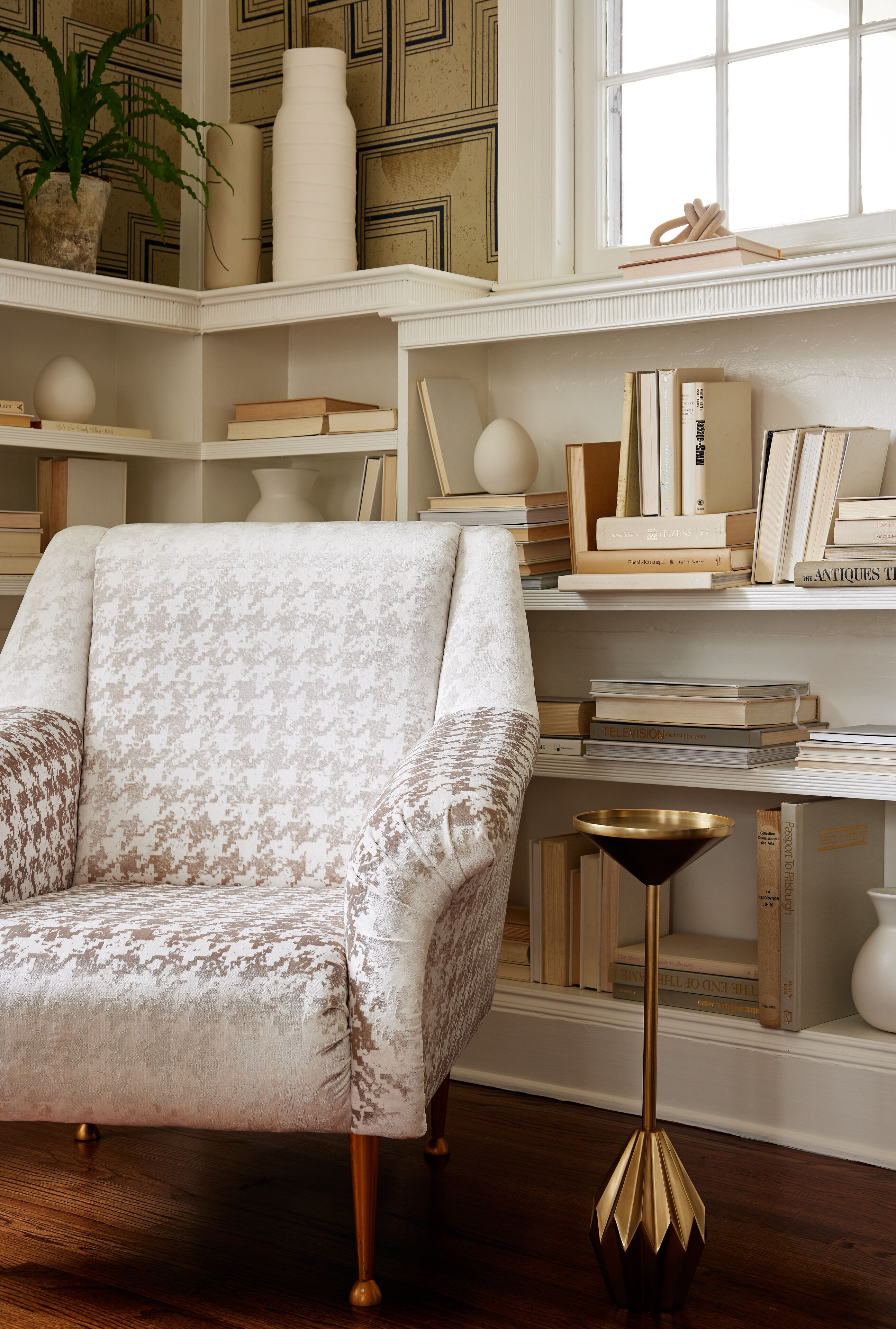 A room with a patterned armchair, a bookshelf with books and decorative items, and a floor lamp.