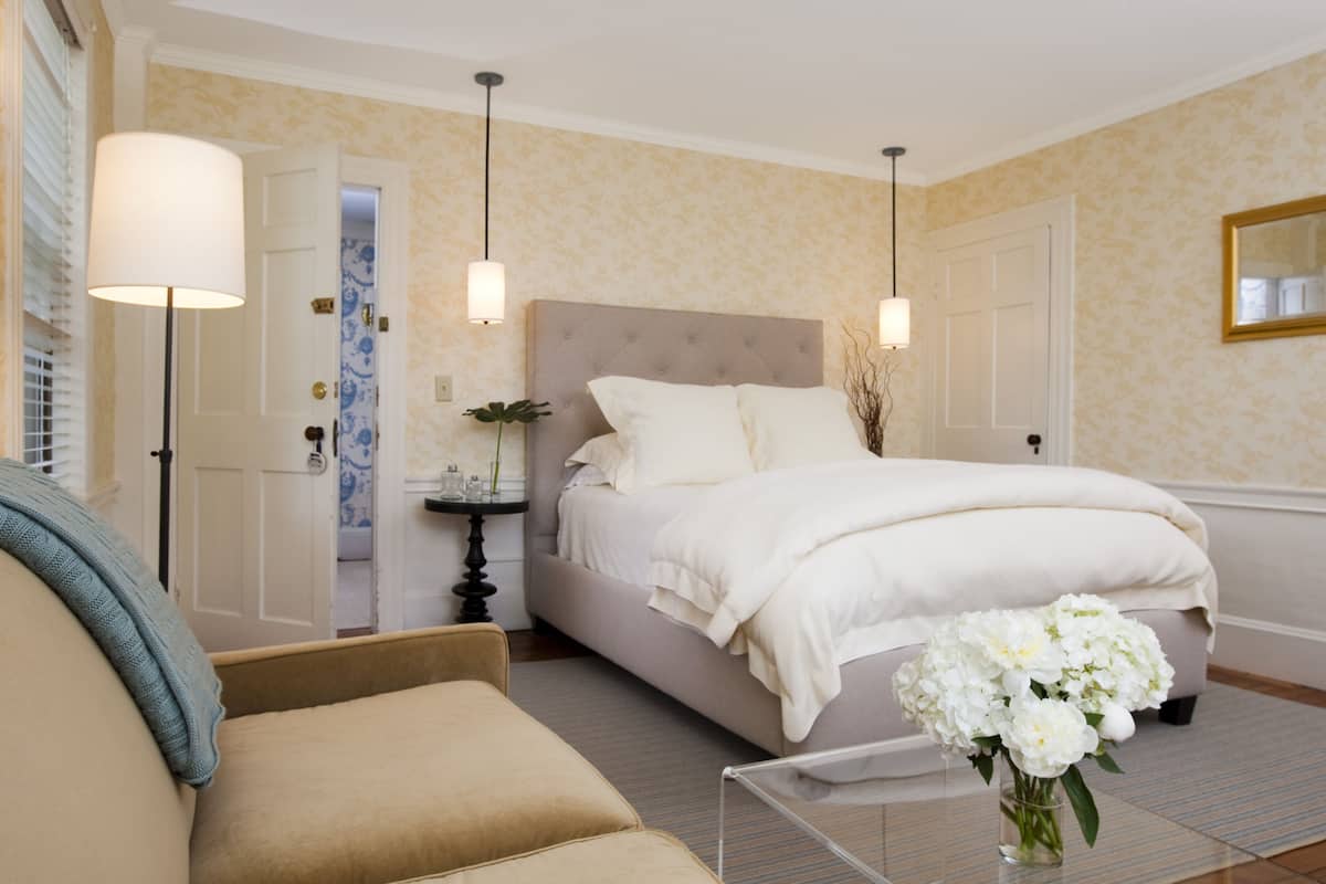 A bedroom with a large bed, bedside tables, a nightstand, a lamp, and a vase with flowers.