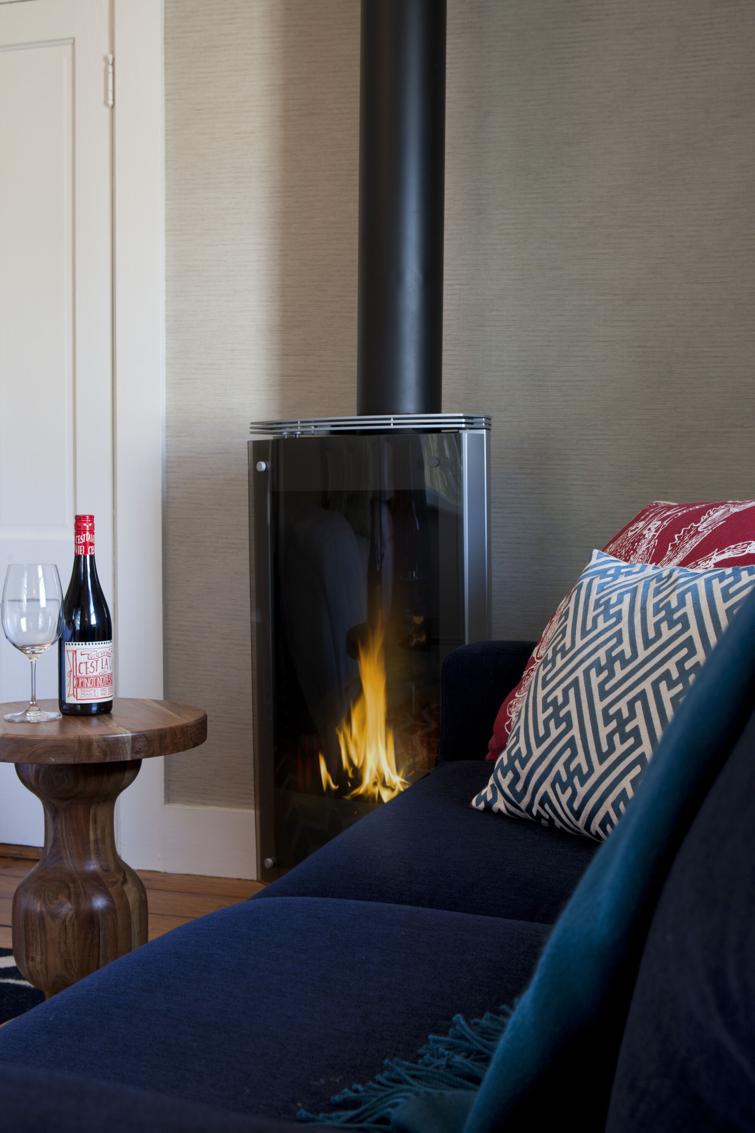 Un salon chaleureux avec une cheminée moderne, une bouteille de vin et un verre posés sur une table en bois.