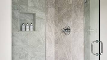 A modern shower enclosure with glass doors, a rain showerhead, and a built-in shelf with toiletries.