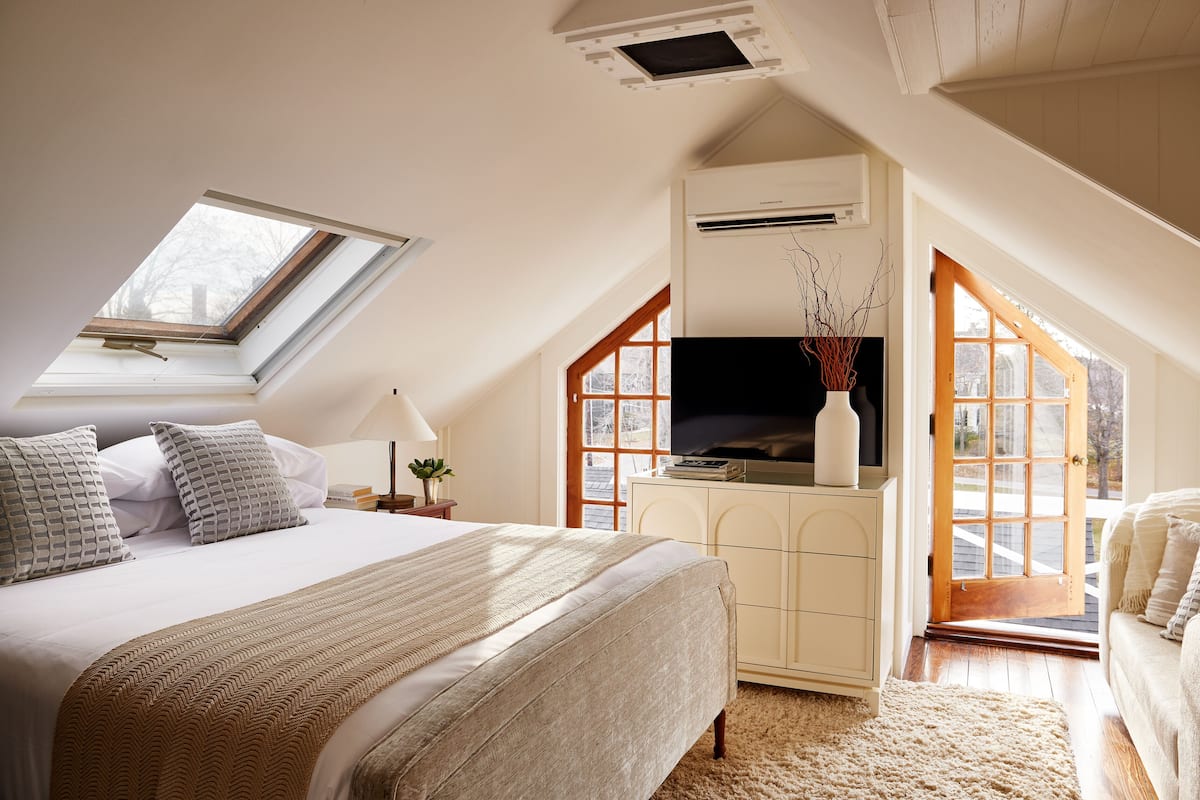 A bedroom with a large bed, a TV, a desk, and a window.