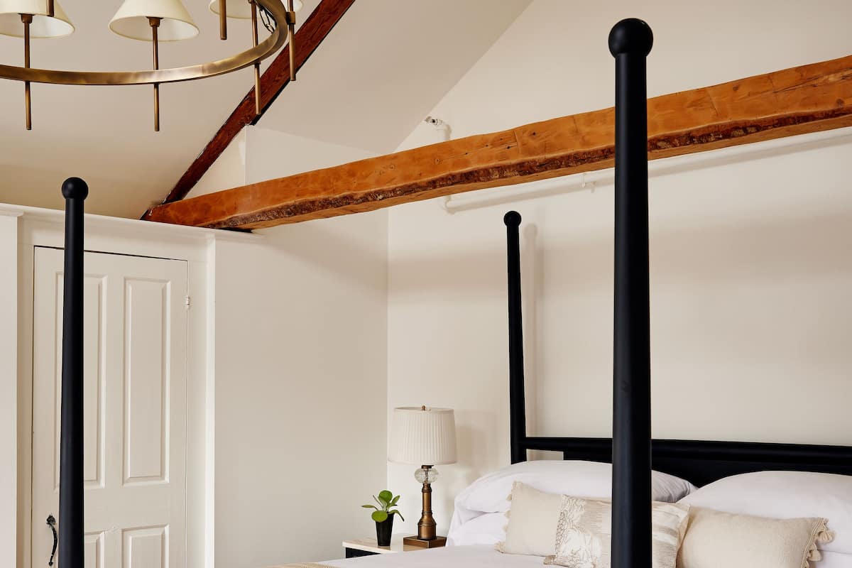 A four-poster bed with a white and beige bedspread, a wooden headboard, and a chandelier with multiple lamps.