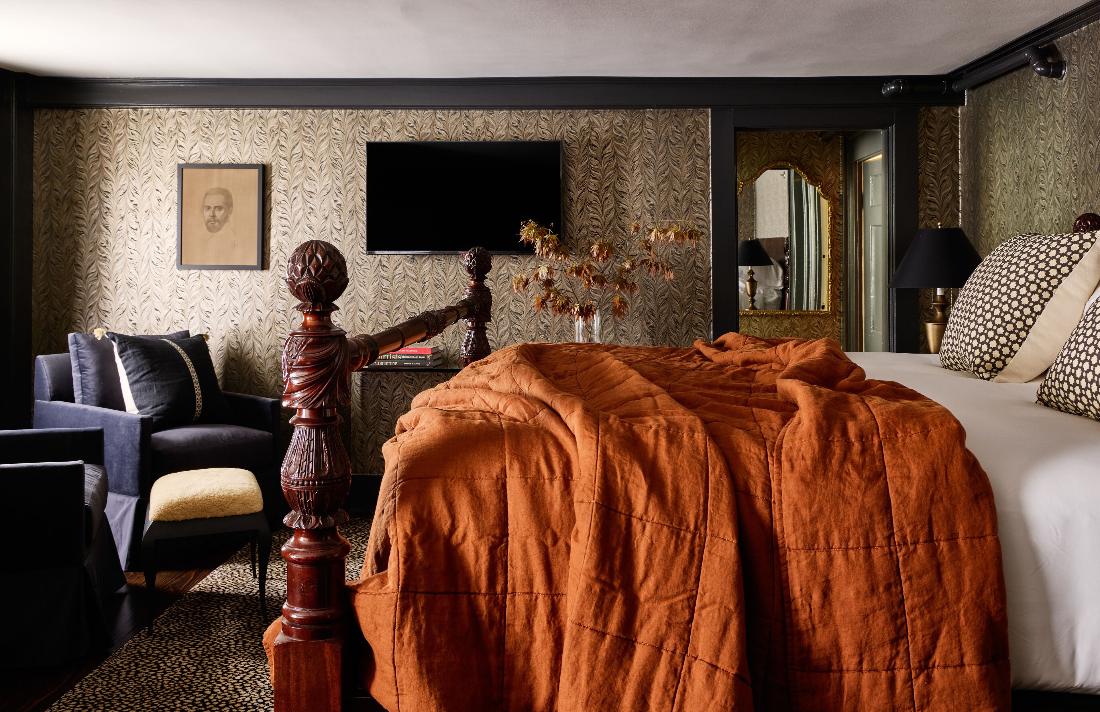 A hotel room with a large bed, a television, a desk with a lamp, and a chair.