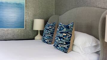 A neatly made bed with white linens, two patterned pillows, a white bedside lamp, and a large abstract painting on the wall.