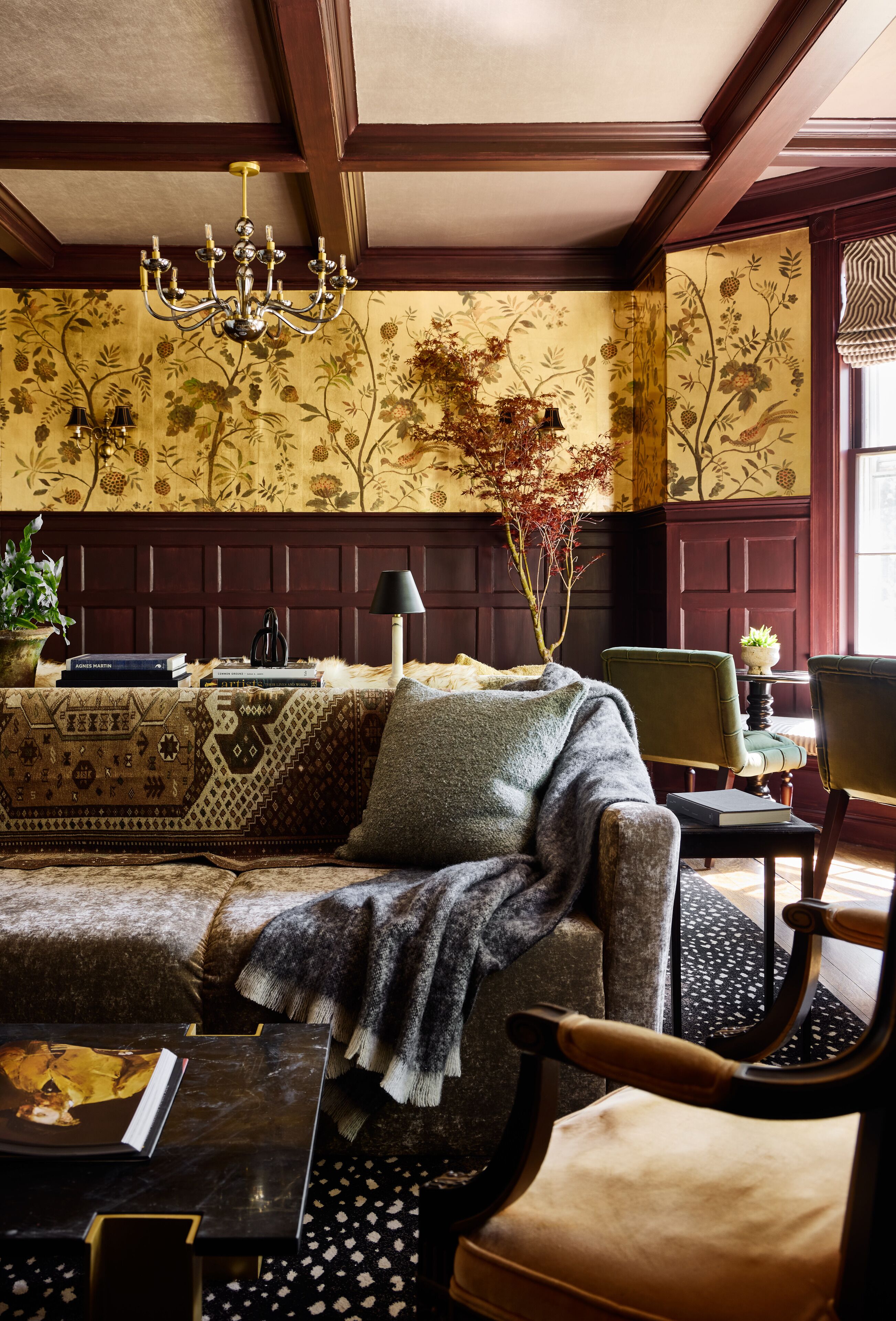 A traditional room with a patterned wallpaper, a chandelier, a sofa, and a dining table with chairs.