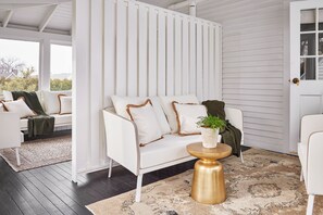 A white sofa with brown trim, a gold side table, and a patterned rug in a room with white walls and a dark wooden floor. - Kennebunkport Captains Collection (Kennebunkport)