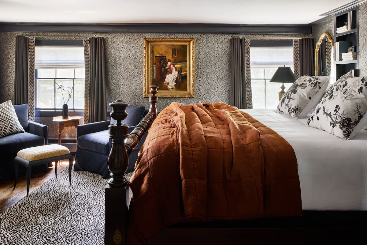 A bedroom with a large bed, a painting on the wall, and a bookshelf.