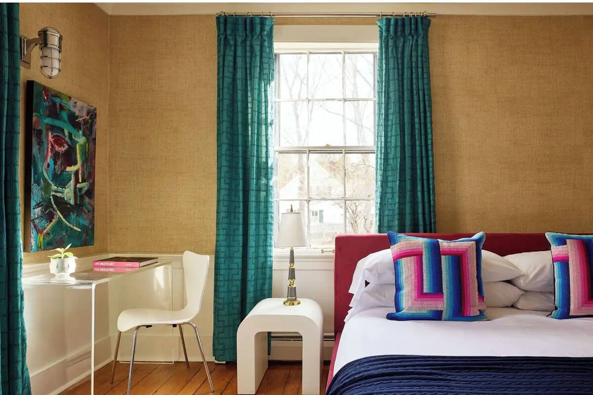 A hotel room with a bed, a desk, a chair, a lamp, and a window with curtains.