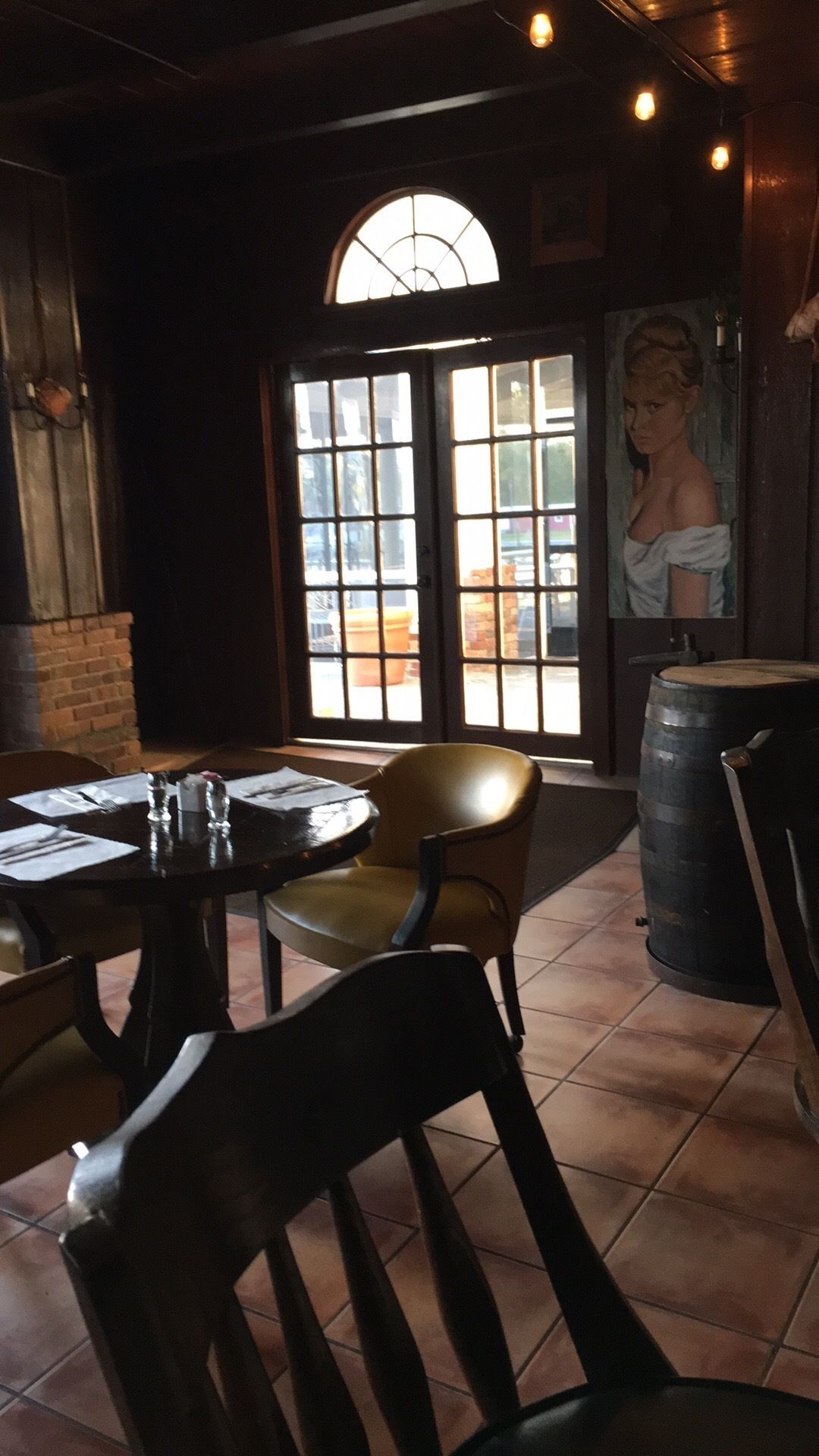 L’intérieur d’un restaurant avec une grande fenêtre, des chaises en bois, une table ronde et un tonneau.
