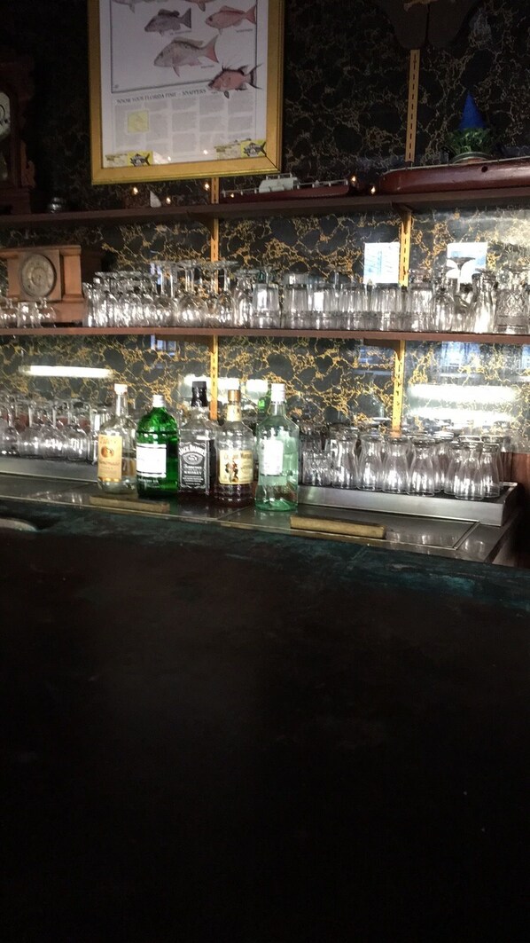 A bar area with shelves of glasses and bottles of liquor. - Rod And Gun Club (Everglades City)