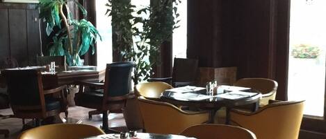 A restaurant with round tables and yellow chairs, potted plants, and a ceiling fan.