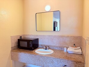 A bathroom with a granite countertop, a black microwave, a sink with a faucet, and a mirror above the countertop.