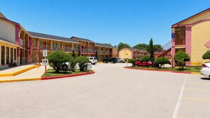 Un motel de varios pisos con una zona de estacionamiento central, una señal de límite de velocidad y una acera roja.