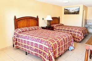 Habitación de hotel con dos camas de madera, una mesita de noche con lámpara, un aparador y un cuadro en la pared.