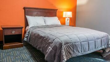 A neatly made bed with a grey quilt, a wooden nightstand with a drawer, and a wall-mounted lamp.