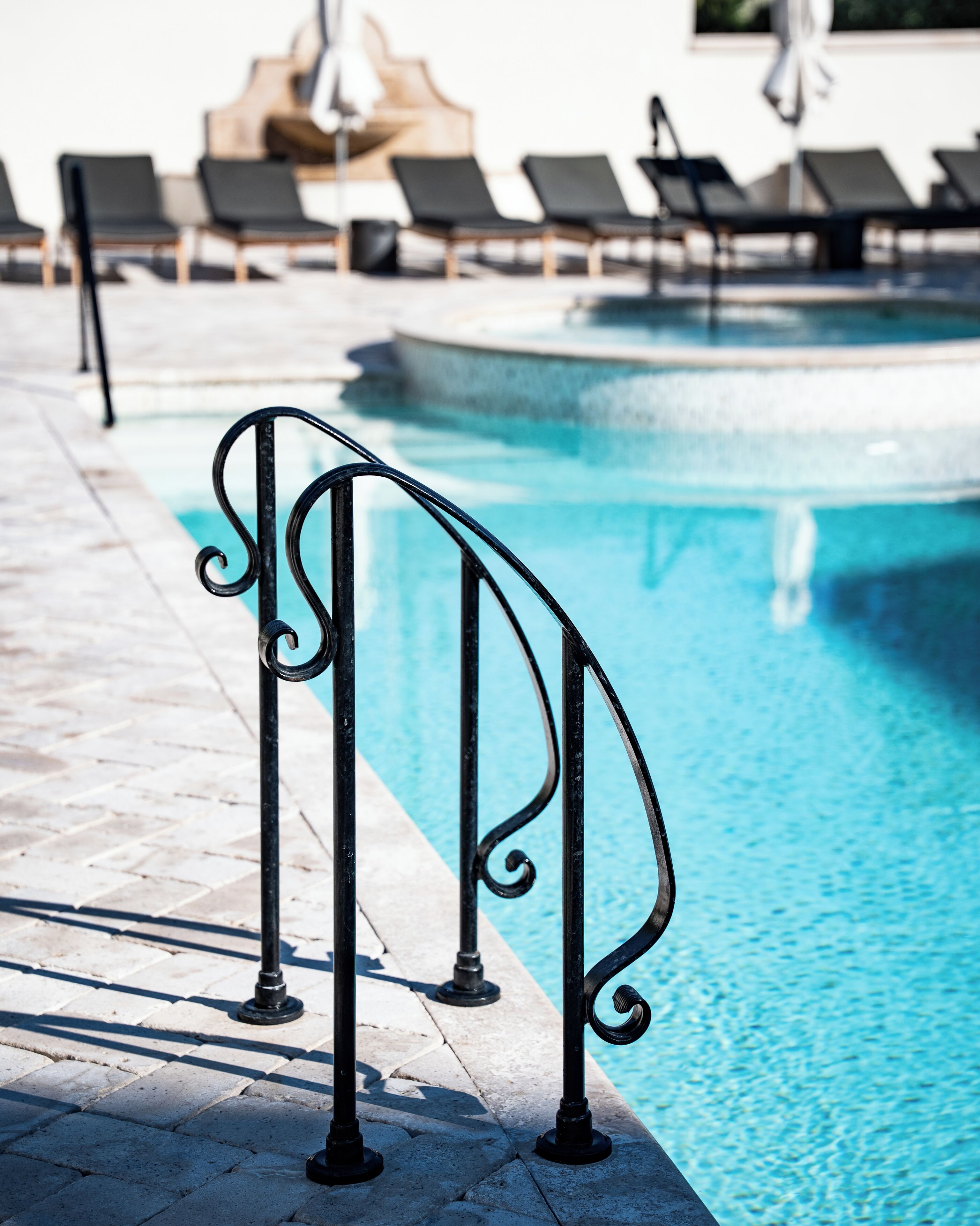 A poolside area with a metal railing, lounge chairs, and a clear blue pool.