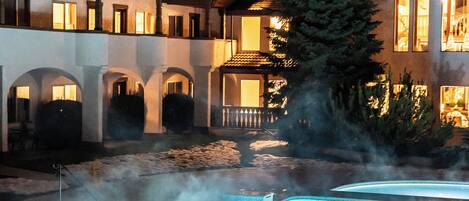 Un hotel con piscina exterior climatizada, varios balcones y un gran árbol de hoja perenne.