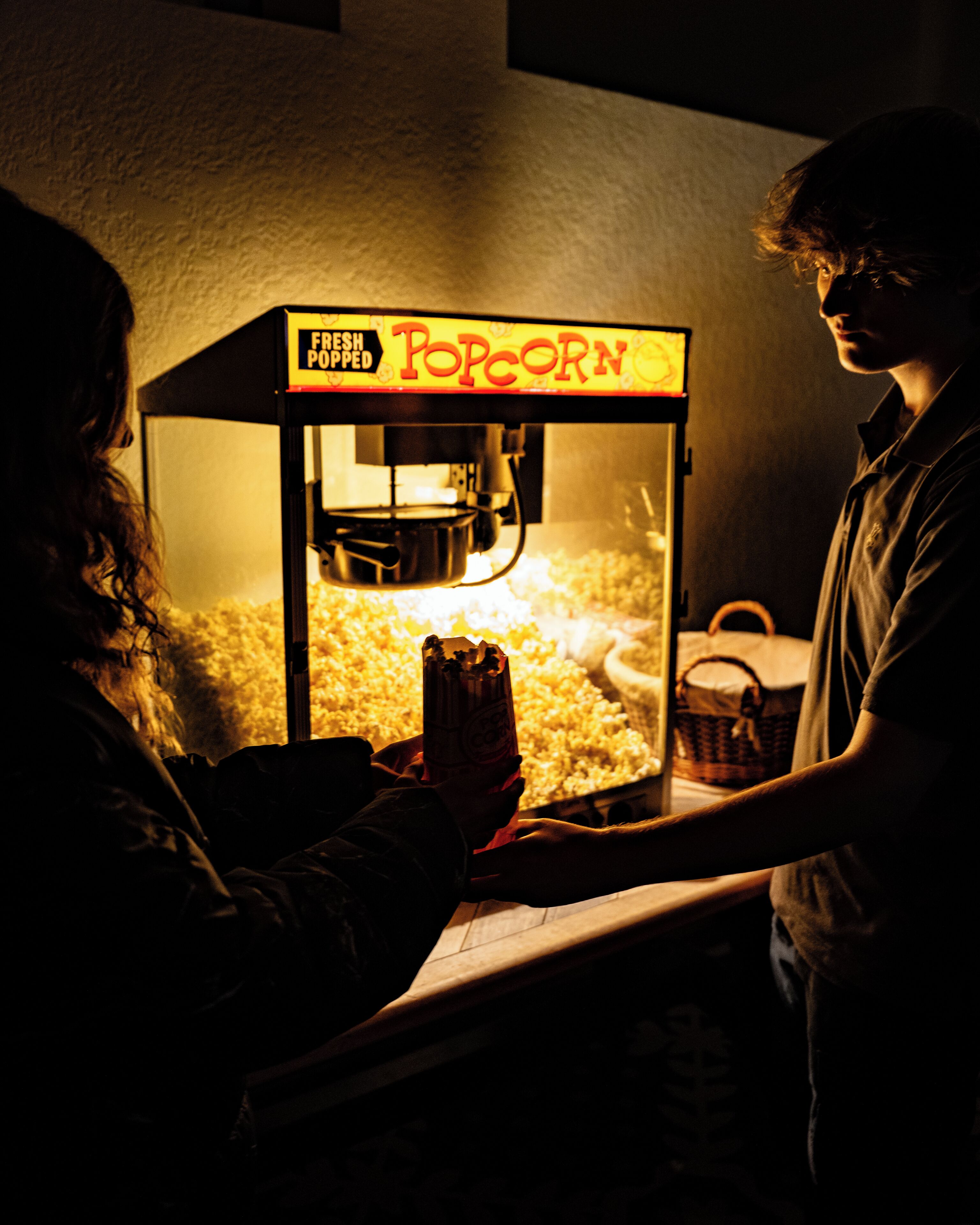 A person operating a popcorn machine with a sign that reads 'Fresh Popped Popcorn.'