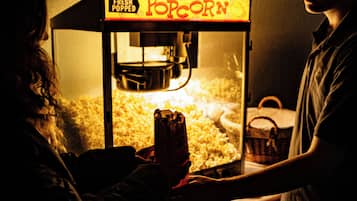 A person operating a popcorn machine with a sign that reads 'Fresh Popped Popcorn.'