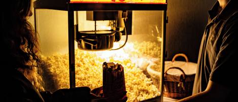 A person operating a popcorn machine with a sign that reads 'Fresh Popped Popcorn.'
