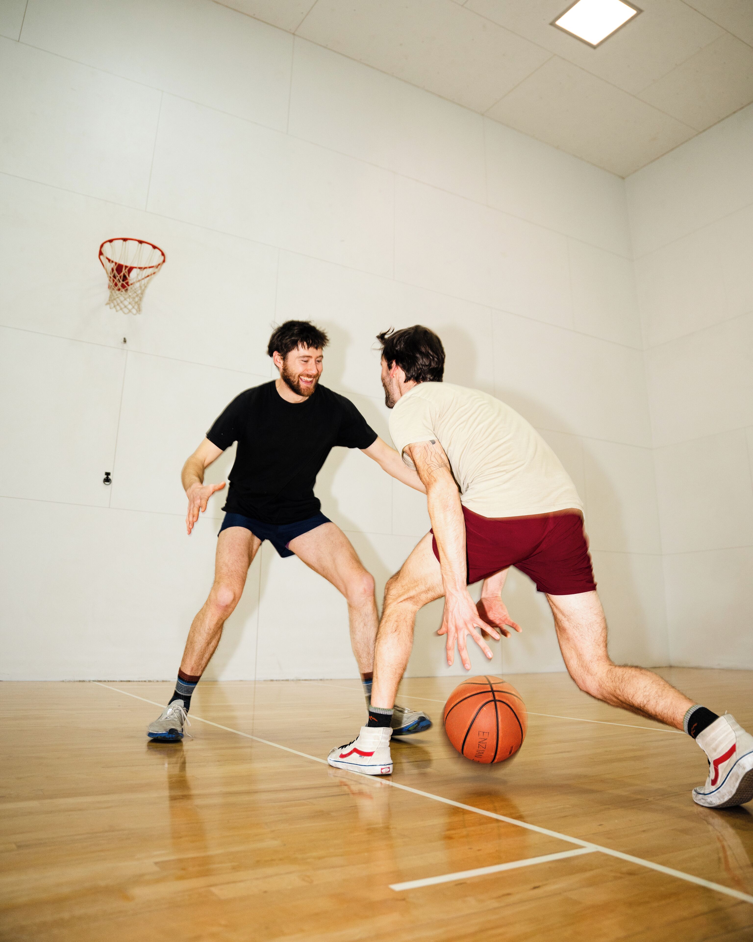 Two people playing basketball in an indoor court with a basketball hoop.