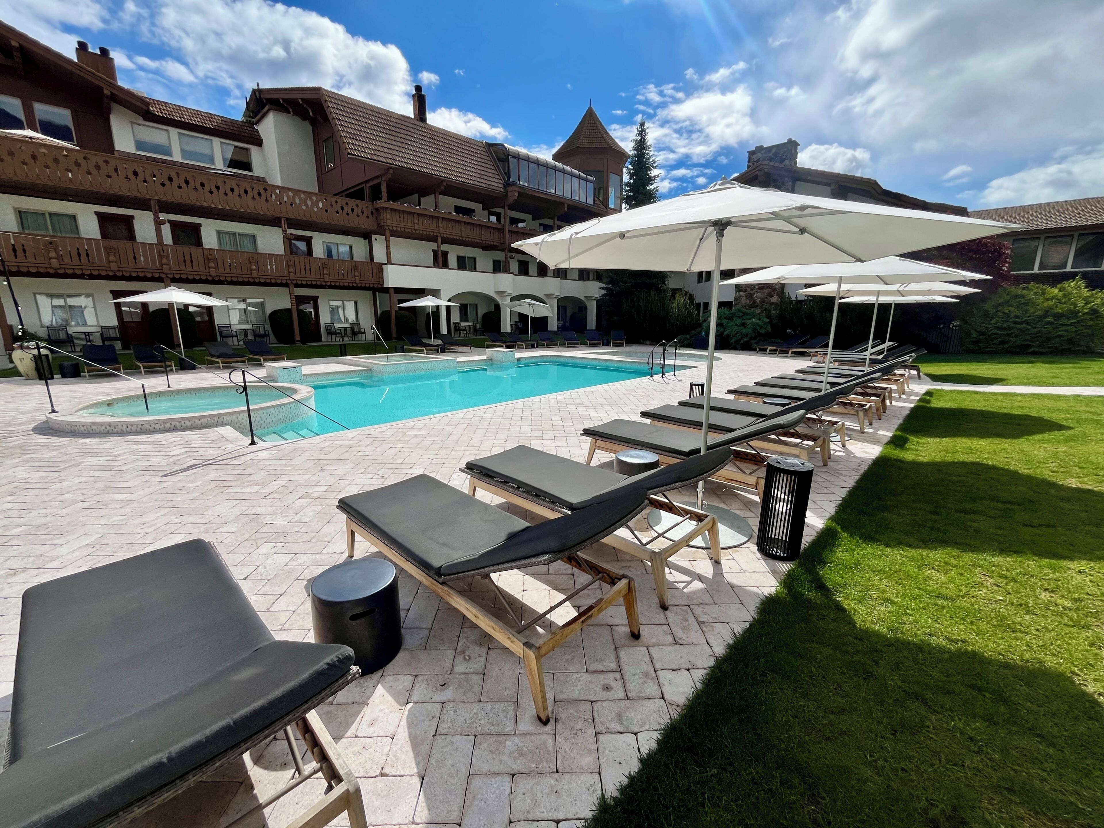 Un área de piscina con sillones de descanso y sombrillas, una piscina y un edificio con balcones.