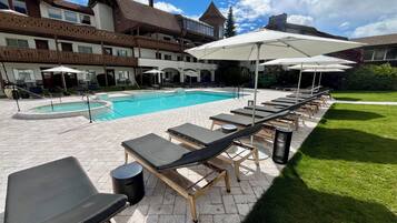 A pool area with lounge chairs and umbrellas, a swimming pool, and a building with balconies.