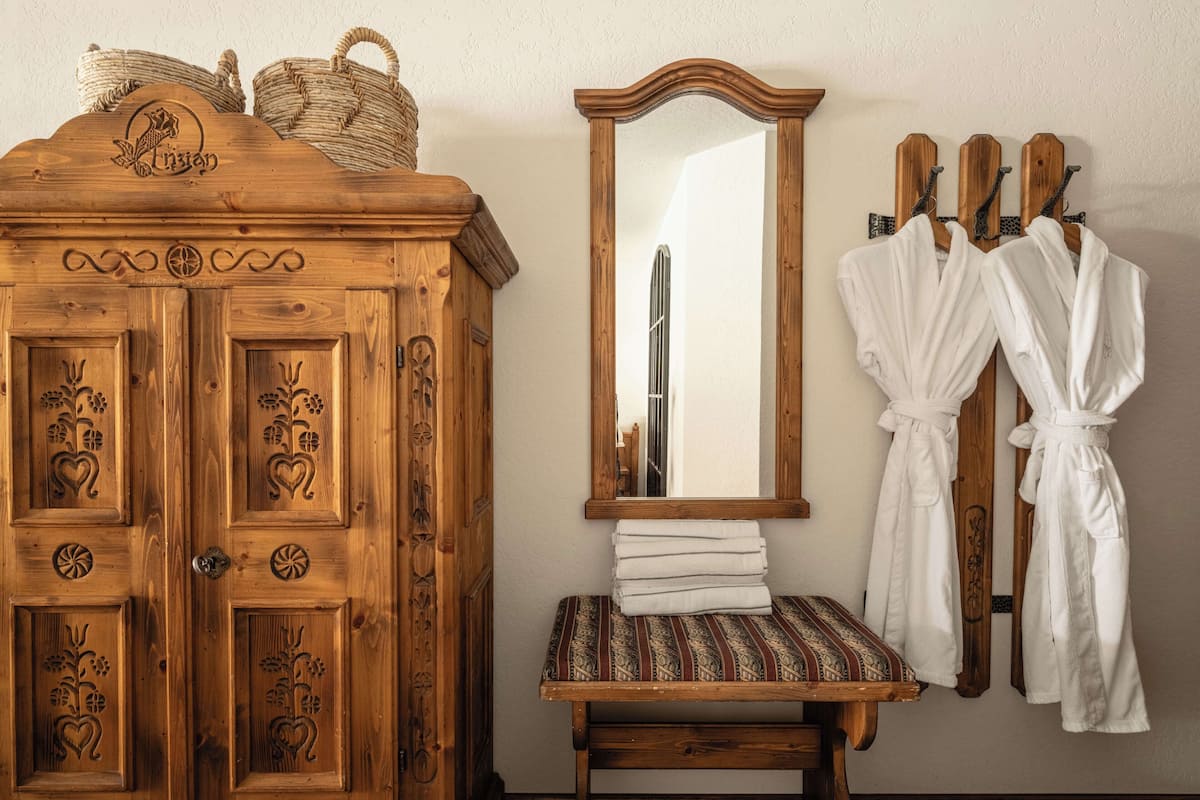 Un armario de madera con diseños florales tallados, un espejo y dos albornoces blancos colgados en ganchos.