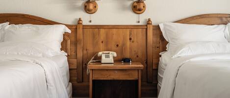 A double room with two wooden beds, a nightstand with a telephone and clock, and two wall-mounted lamps.