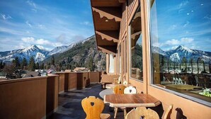 A balcony with a view of snow-capped mountains, wooden furniture, and a glass door.