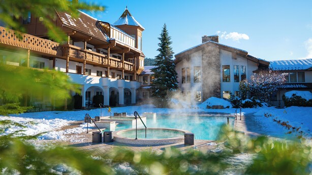 A resort with a hot tub, snow-covered ground, and a large building with balconies.