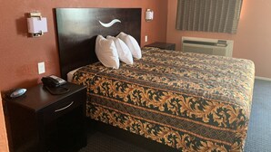 A hotel room with a large bed, a bedside table with a phone, and a wall-mounted light fixture.