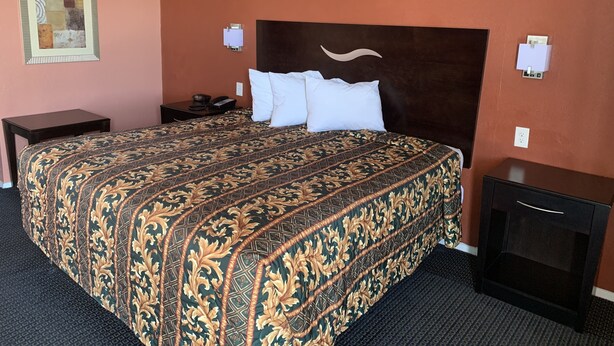 A hotel room with a large bed, a nightstand, a dresser, and a wall-mounted telephone.