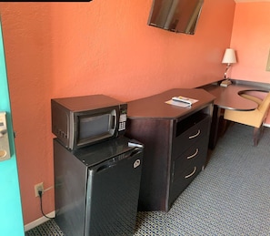 A compact kitchenette with a microwave and refrigerator, a small table with a magazine, and a chair.