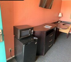 A compact kitchenette with a microwave and refrigerator, a small table with a magazine, and a chair.