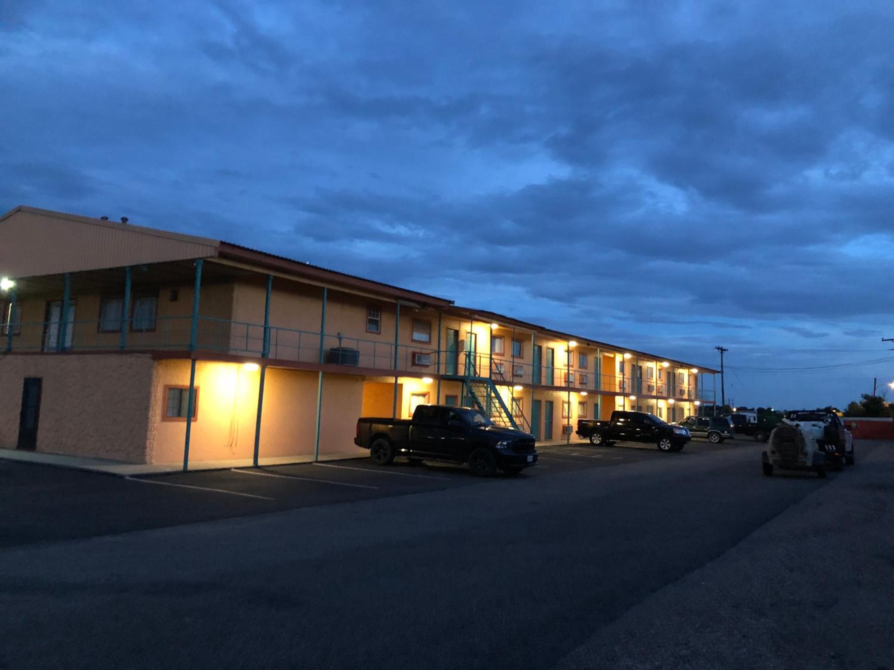 A motel with multiple rooms, a parking lot, and a few vehicles parked.