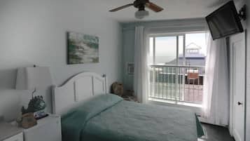 A bedroom with a bed, a nightstand, a ceiling fan, a window with curtains, and a view of a building outside.