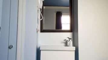 A bathroom with a white vanity, a mirror above it, and a hairdryer on the wall.