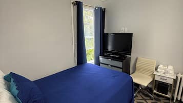 Une chambre d’hôtel avec un lit, une télévision, une chaise, un bureau et une fenêtre avec des rideaux.