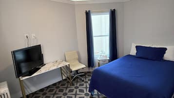 A hotel room with a bed, a desk with a chair, a television, and a ceiling fan.