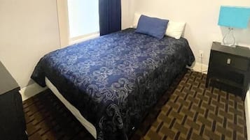 Une chambre à coucher avec un lit, une fenêtre avec des rideaux, une table de chevet avec une lampe et un tapis à motifs.