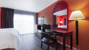 A hotel room with a bed, a desk, a chair, a TV, a lamp, and a large mirror. - Pullman Garden Inn (Pullman)