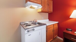 A compact kitchen with a stove, sink, and wooden cabinets. - Pullman Garden Inn (Pullman)